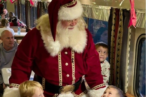 Santa Claus in a train with festive lights, surrounded by smiling children.