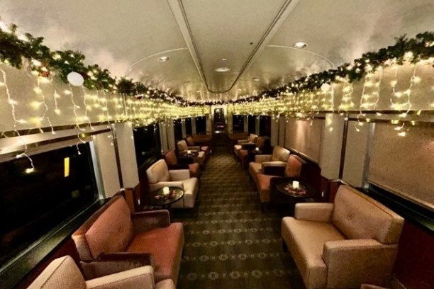 Train car interior with festive lights and garlands, cozy seating arrangement.