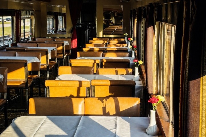 Sunlit train dining car with empty tables and small flower vases.